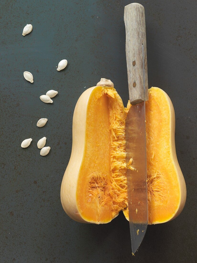 A halved butternut squash with a knife and seeds