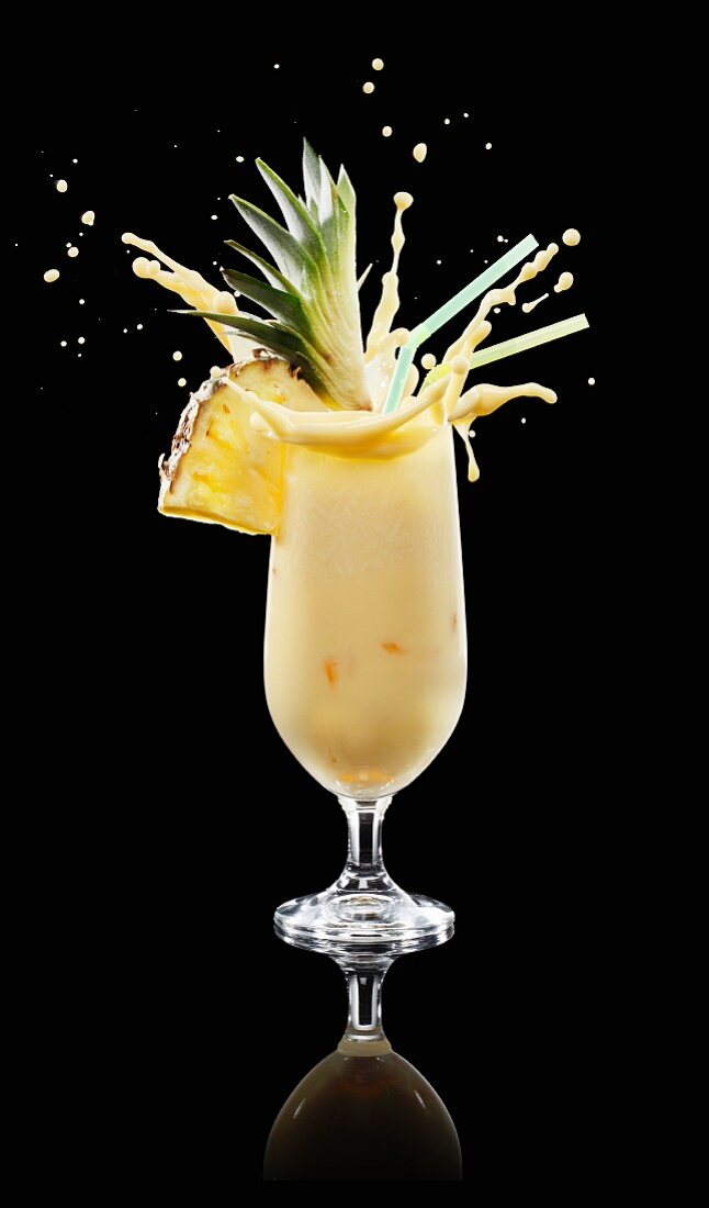 A splashing pina colada in a glass against a black background