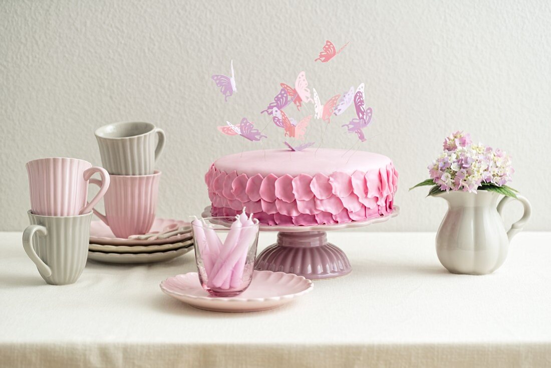 Biskuittorte mit Buttercreme und mit rosa Fondant überzogen, mit Blütenblättern aus Fondant und Schmetterlingen aus Papier dekoriert