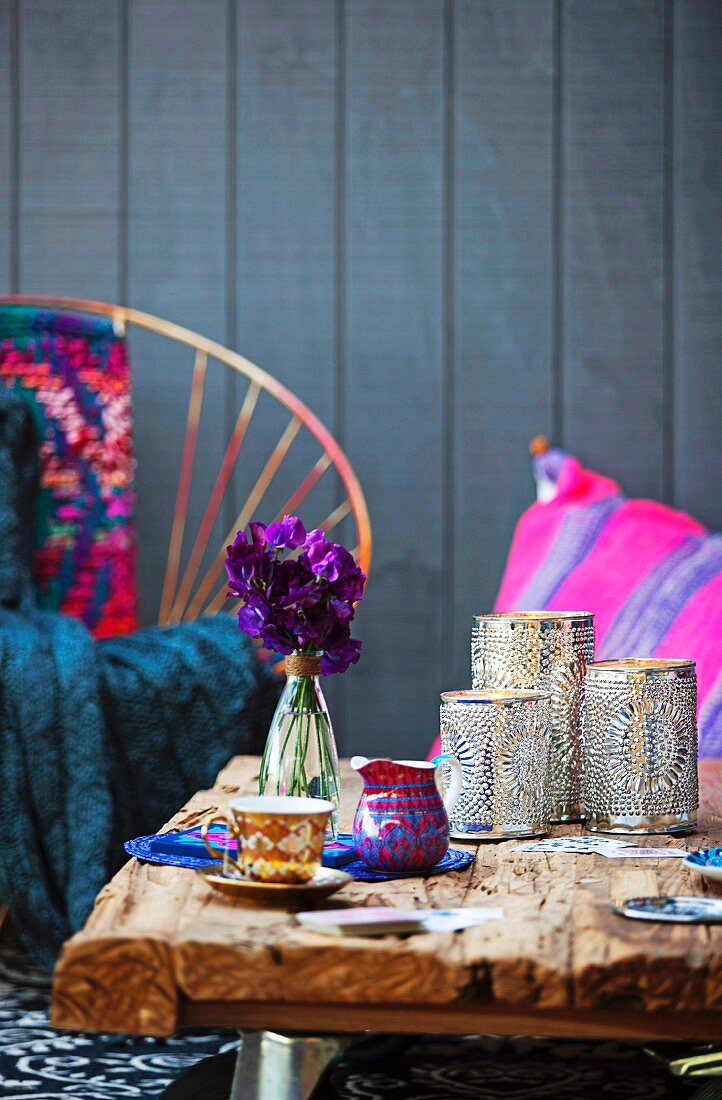 Moroccan silver lanterns and mocha cup on rustic wooden table; colourful scatter cushions and wood cladding in background