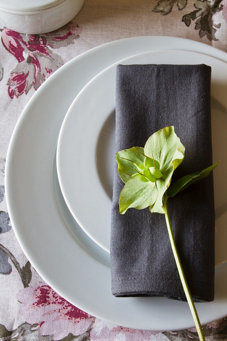 A place setting with two plates and a grey napkin decorated with a green winter rose