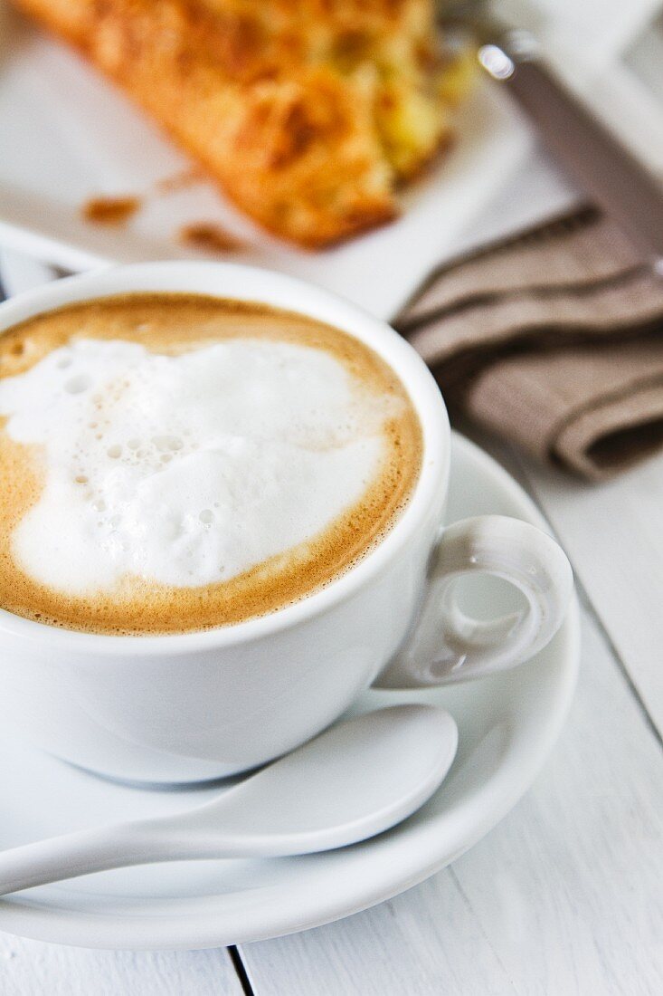 Cappuccino in Tasse mit Milchschaum, dahinter Apfeltasche