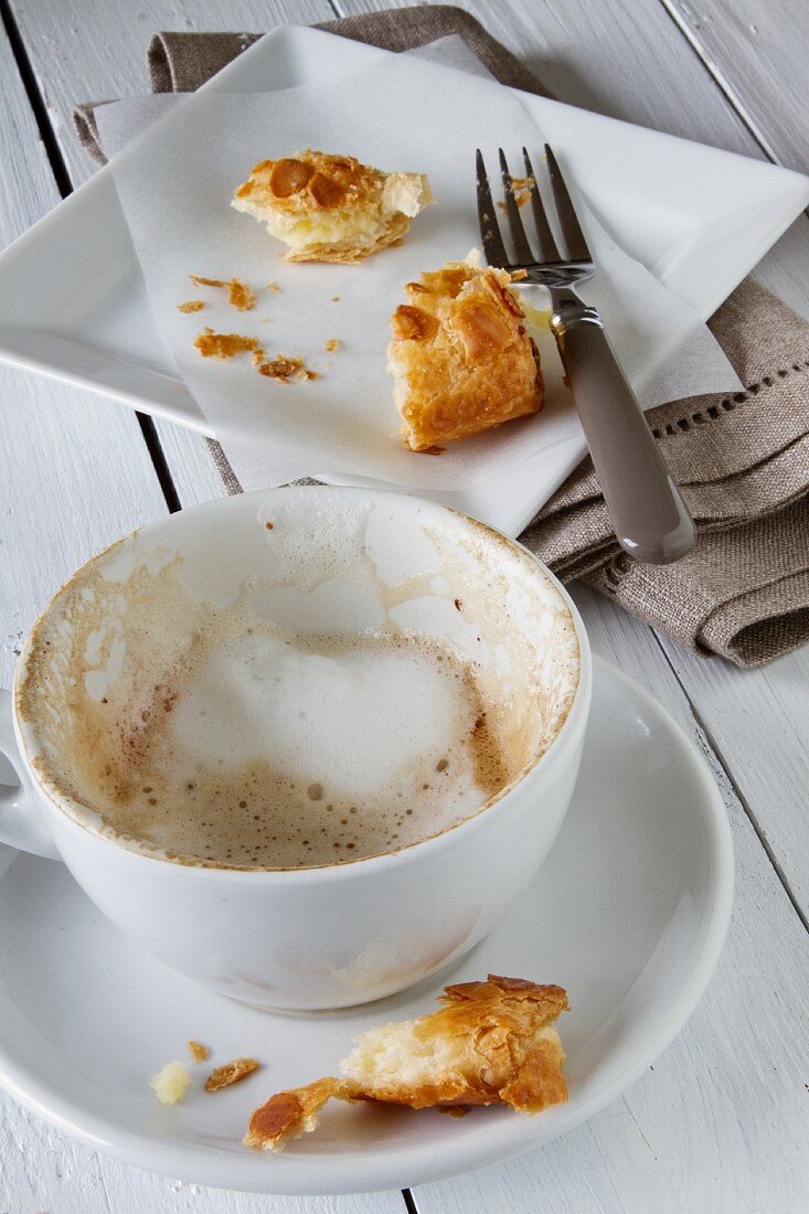 Cappuccinotasse mit Rest von Milchschaum und fast aufgegessene Apfeltasche