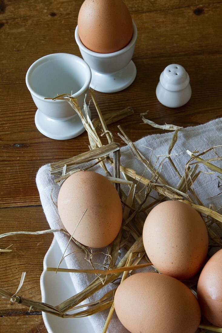 Braune Eier mit Stroh auf Teller und in Eierbecher