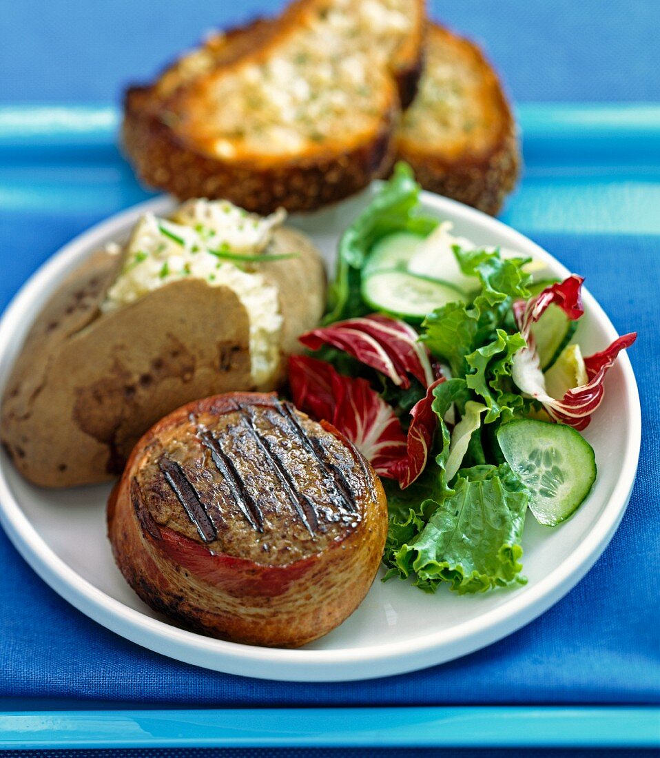 Minced steak wrapped in bacon served with a baked potato and salad