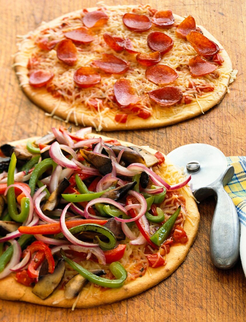 Zwei verschiedene Pizzen mit Pizzaschneider auf Holzbrett