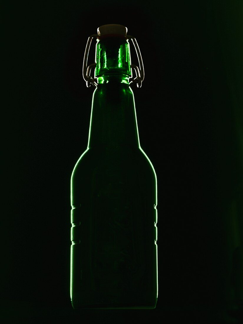 Grüne Bierflasche mit Bügelverschluß im Gegenlicht vor schwarzem Hintergrund