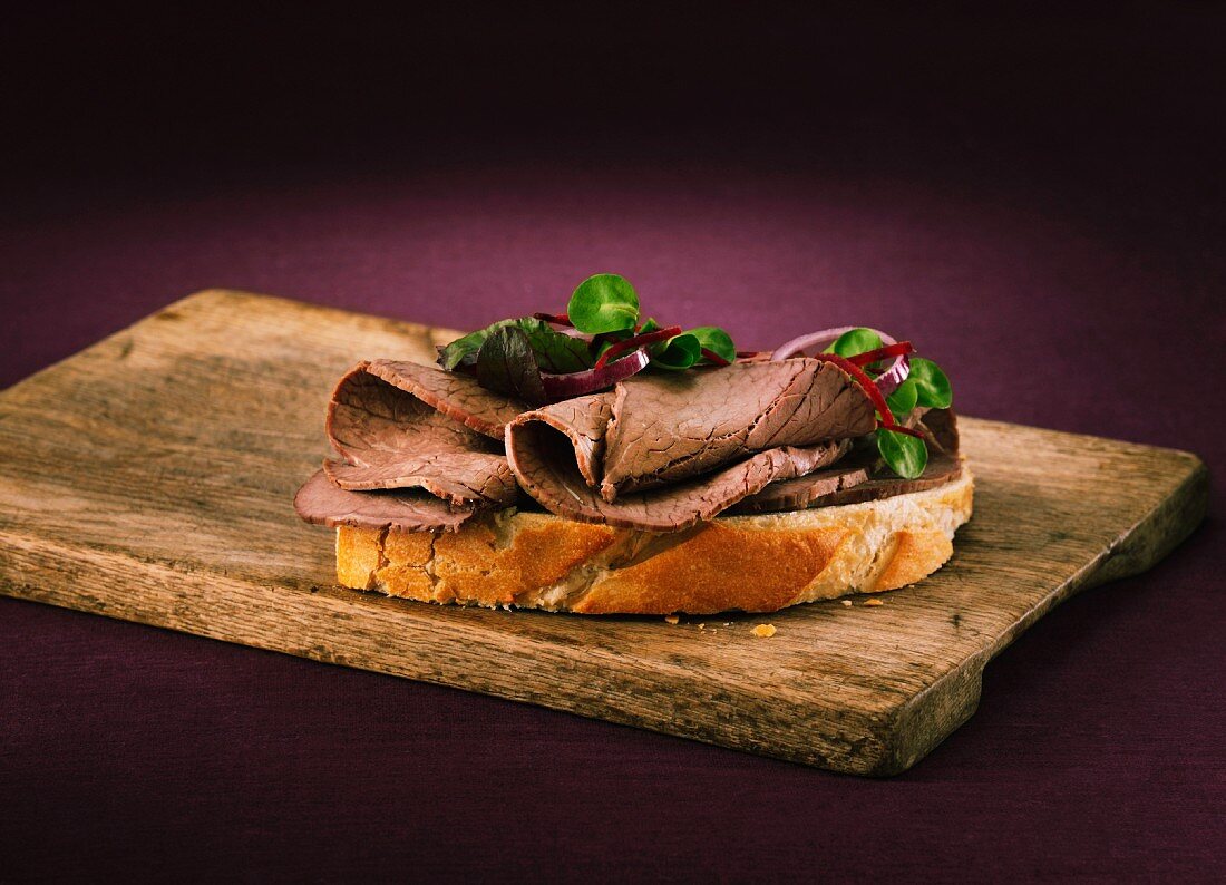 A slice of white bread topped with roast beef on a wooden board