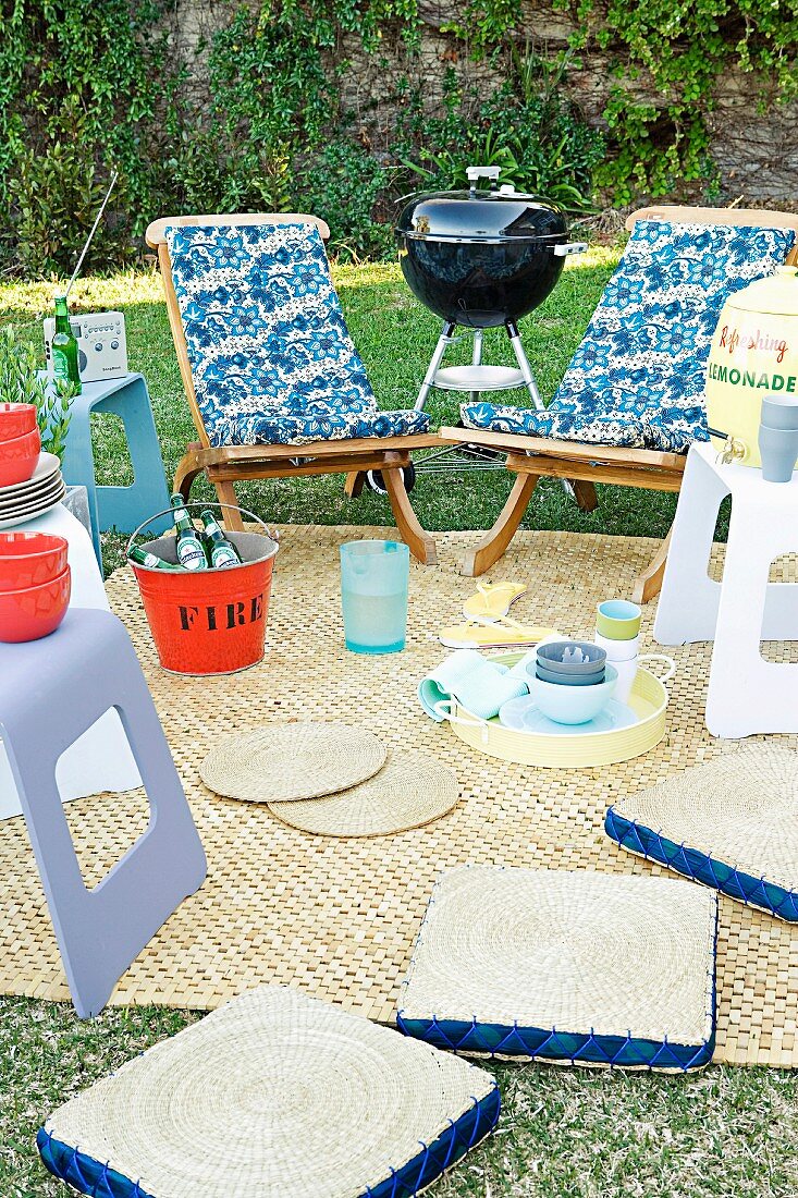 Garden picnic - various chairs and stools around blanket and mobile barbecue on lawn