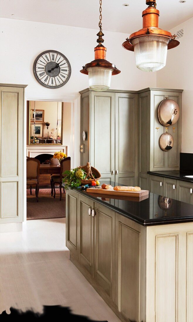 Country-house kitchen with pale grey cupboards; open doorway in background with view into living room beyond