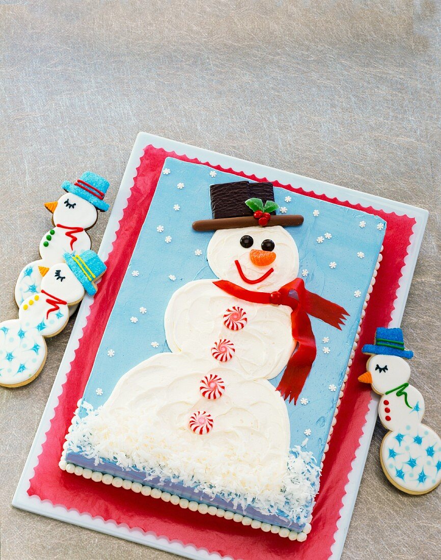 A rectangular cake decorated with a snowman with snowman biscuits