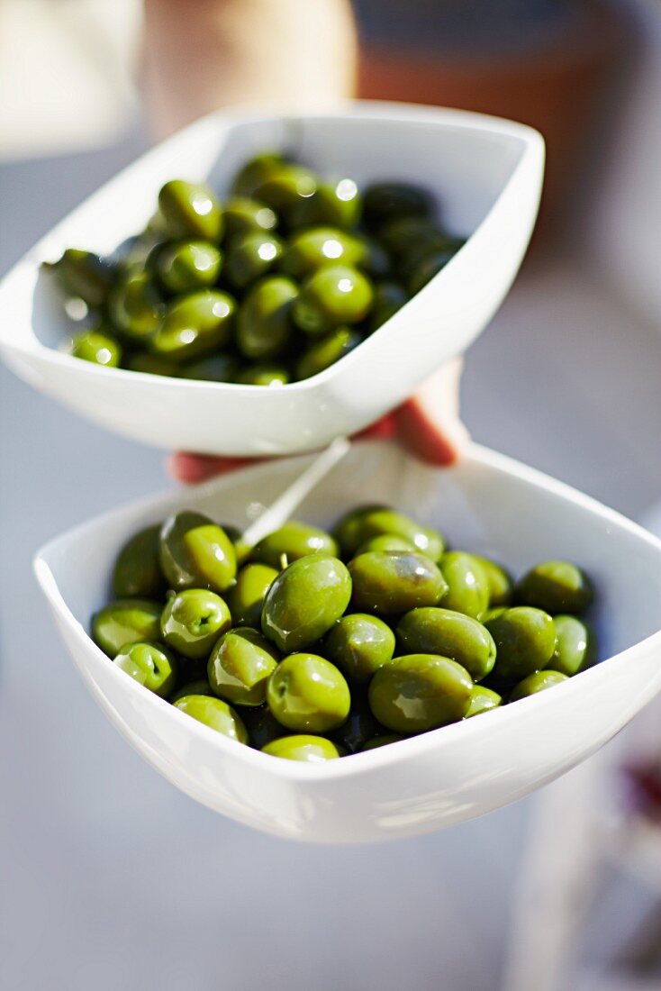 A hand holding bowls of green olives