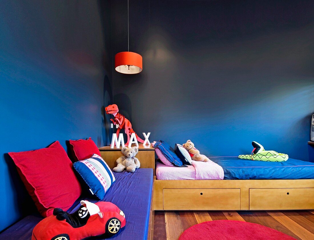 Kinderbett und Sitzbank mit Kissen und Spielzeug in dunkelblau getönter Zimmerecke
