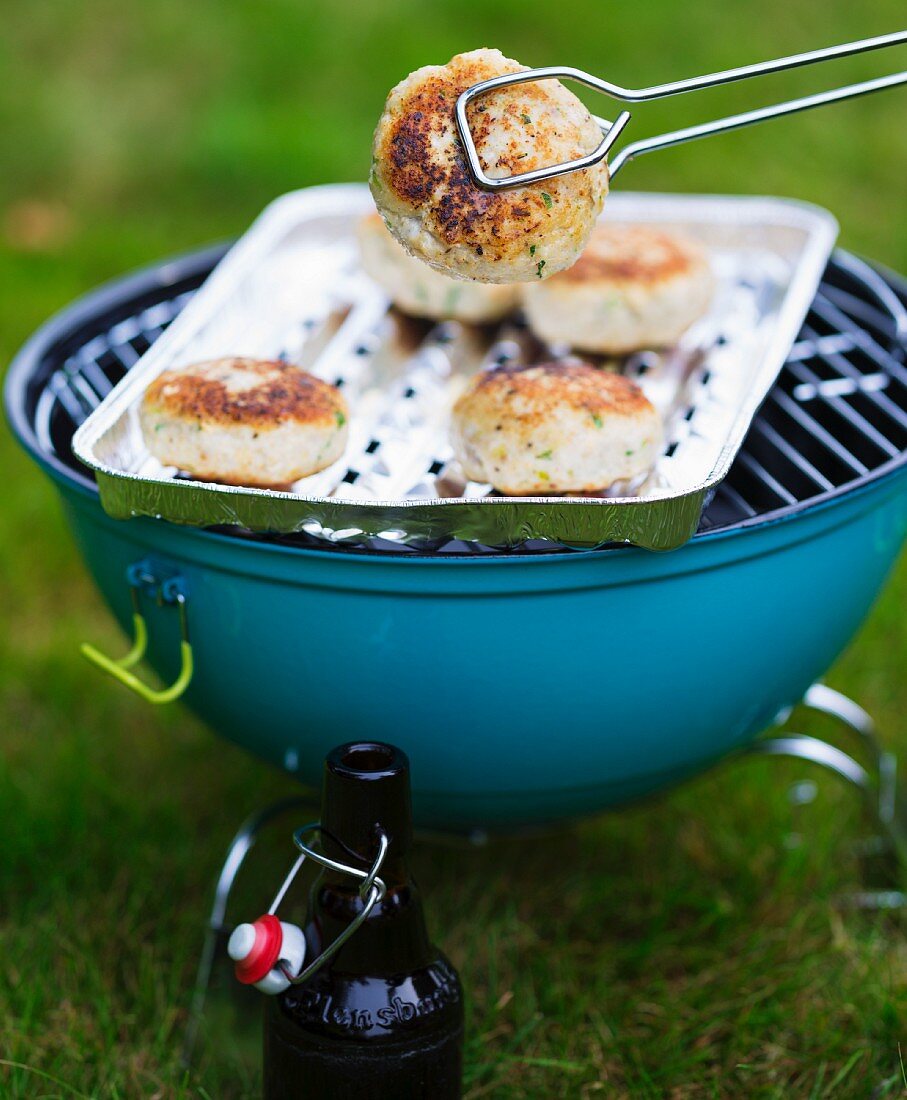 Fish cakes with coriander on an aluminium tray on a barbecue
