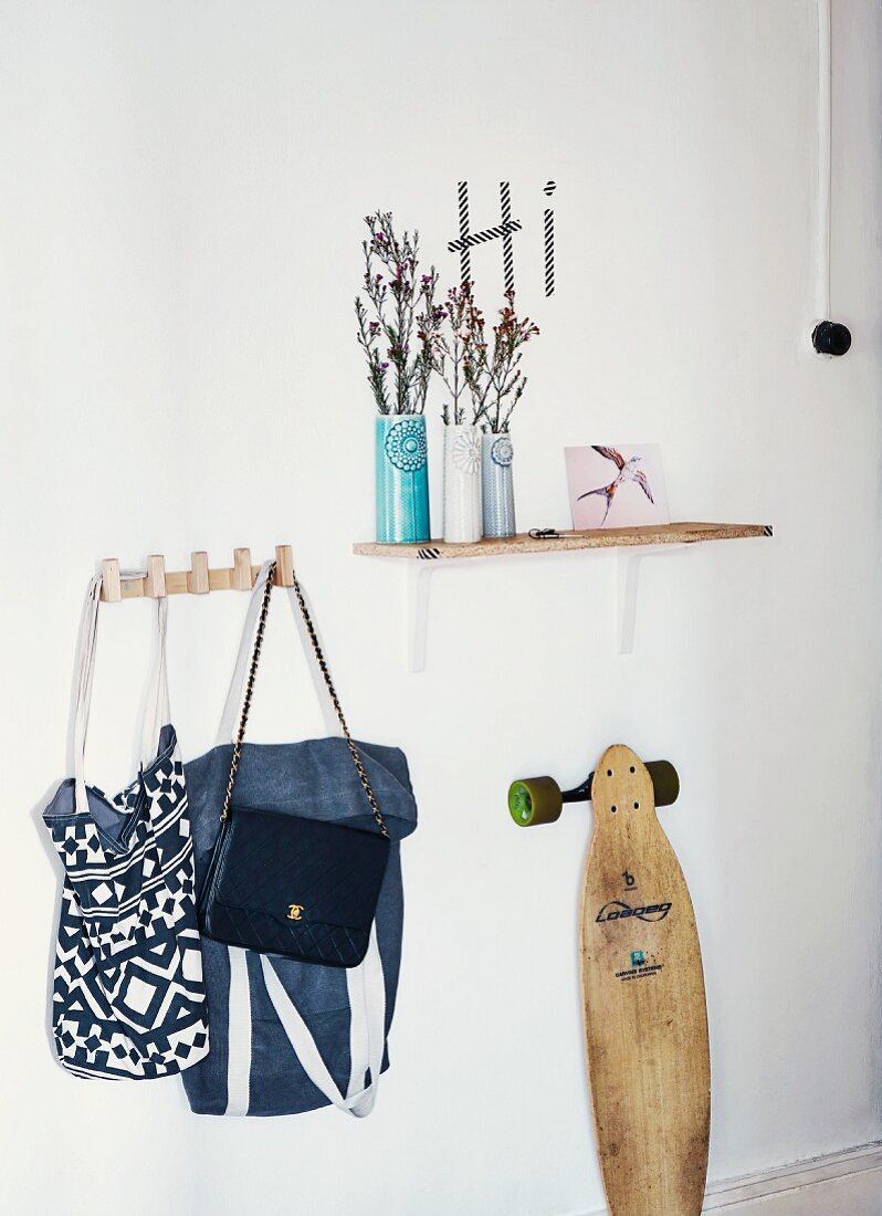 Still-life cloakroom arrangement with ceramic vases on wall-mounted shelf, collection of bags on hooks and vintage skateboard