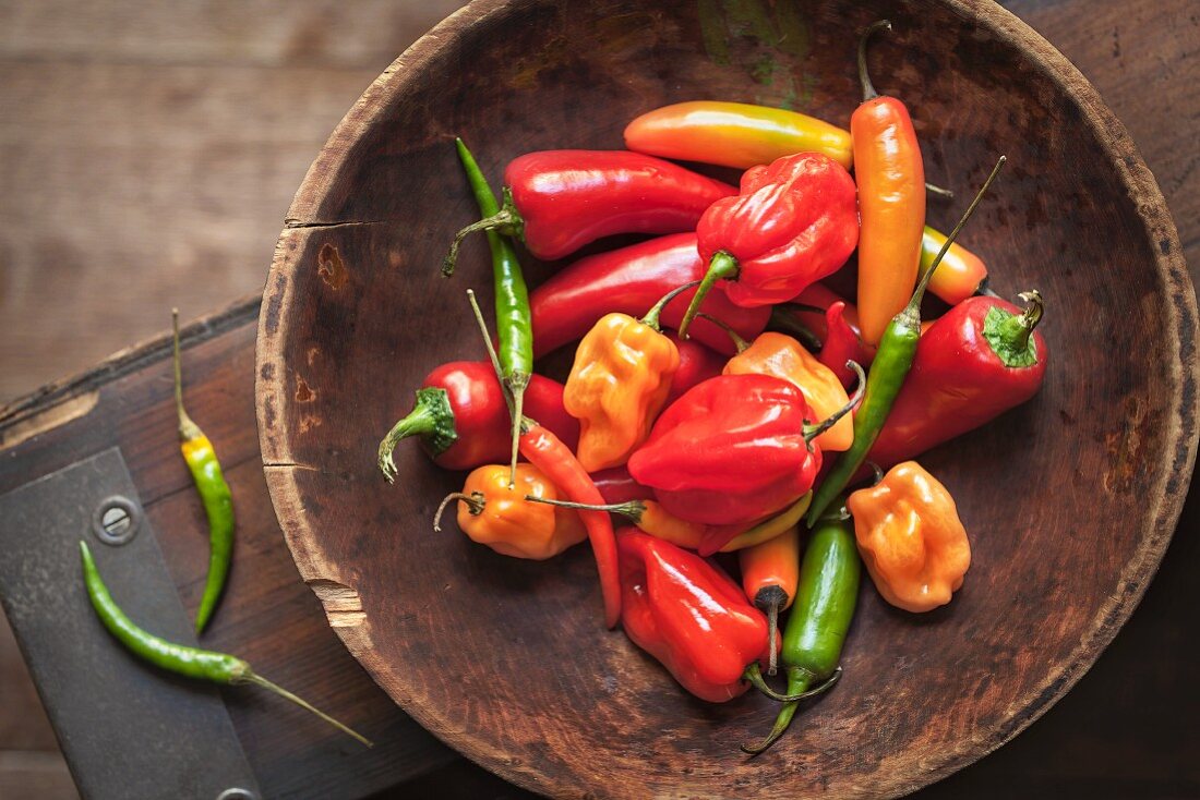 Various chilli peppers and peppers in a wooden bowl