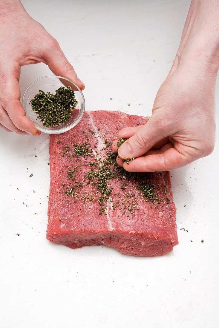 Herbs being strewn onto a slice of raw beef