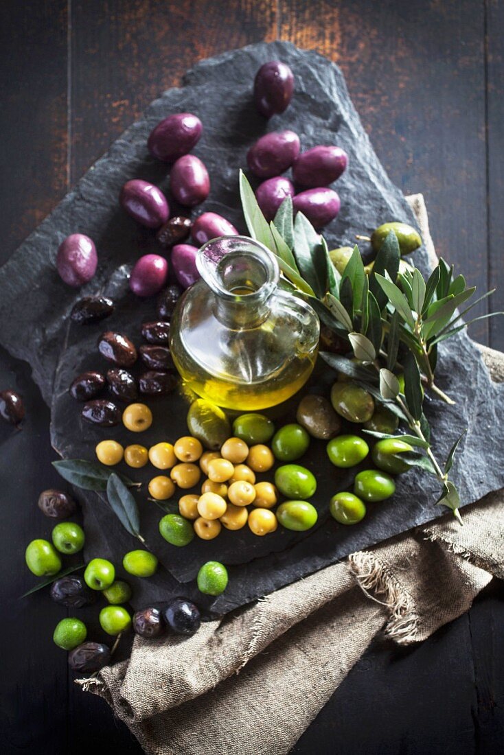 A carafe of olive oil, various olives and an olive spring on a stone platter
