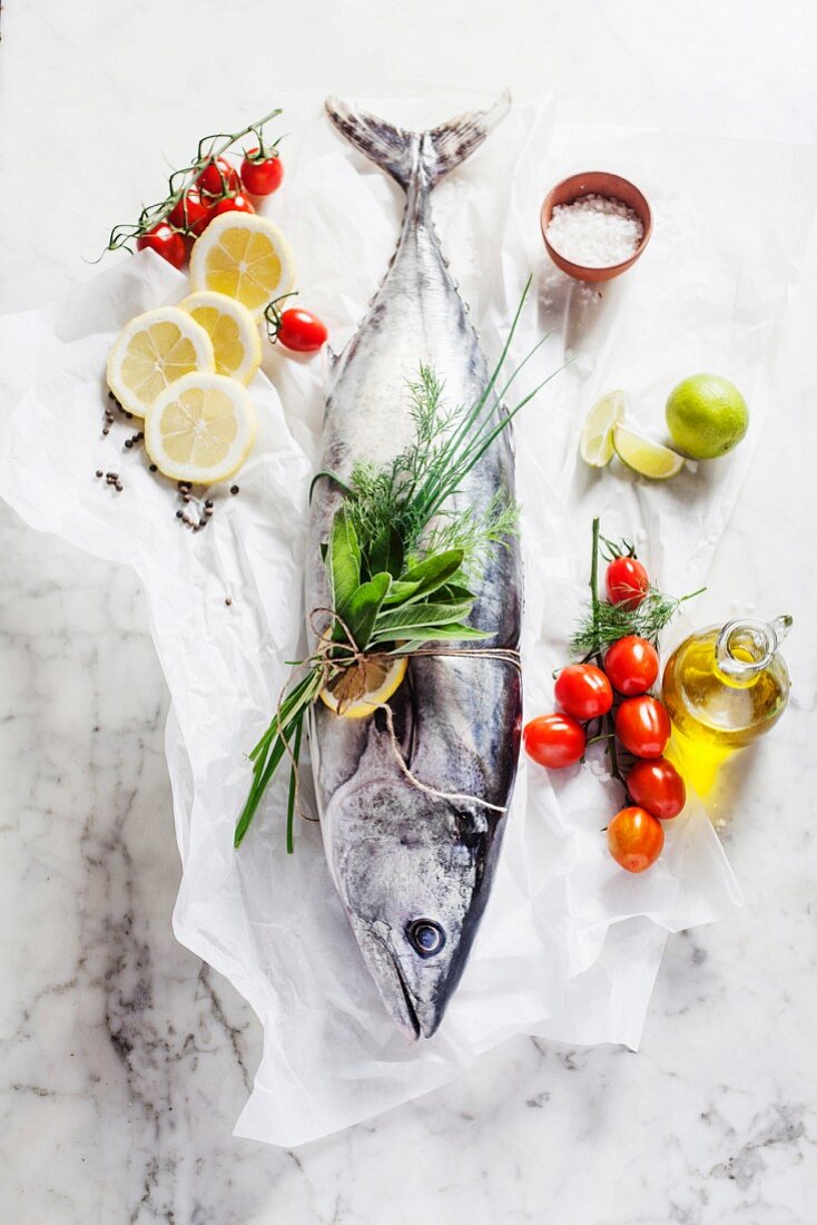 A whole tuna fish, cherry tomatoes, a bunch of herbs, lemons, olive oil and salt