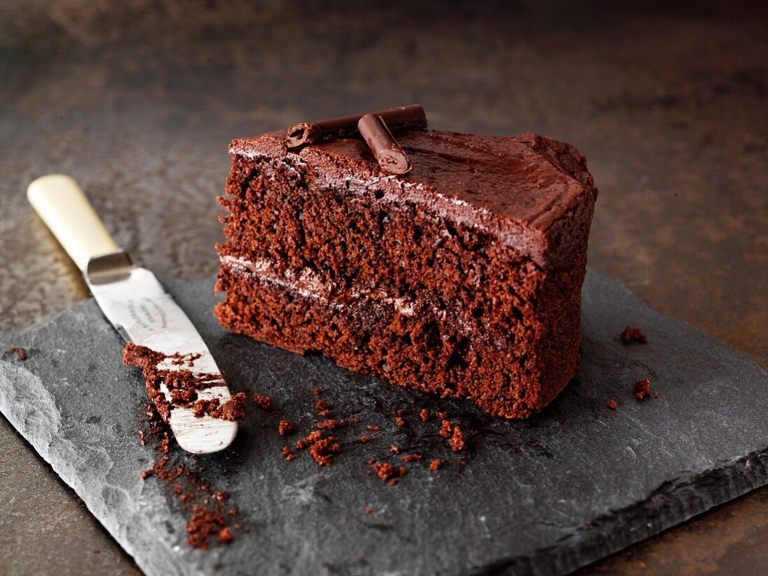 A slice of chocolate cake on a stone platter with a knife