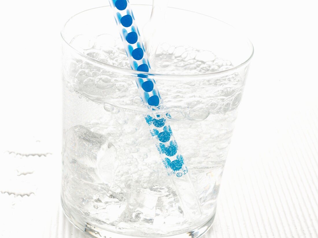 A glass of sparkling mineral water with ice cubes and a straw