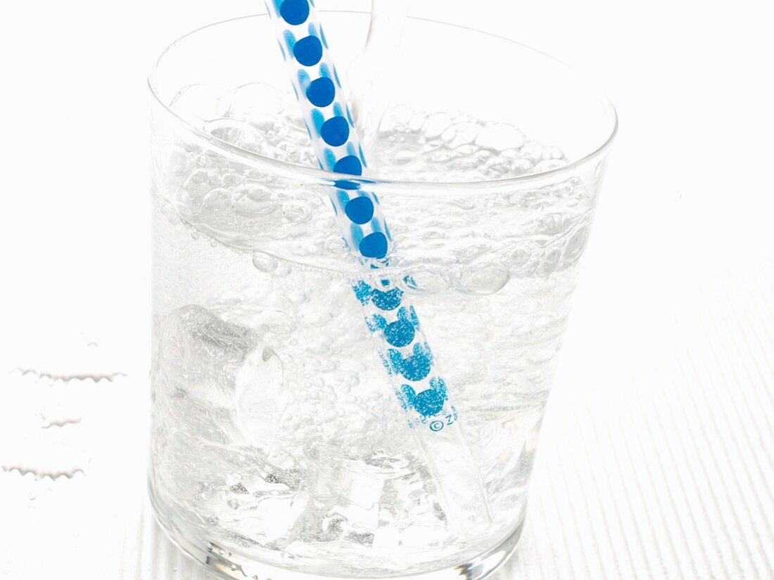 Mineralwasser im Glas mit Eiswürfeln und Strohhalm