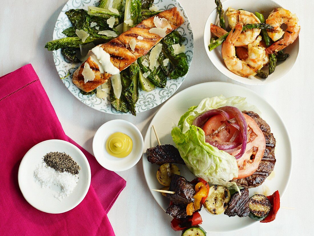 Various barbecue dishes: burger, salmon, prawns, kebabs, asparagus