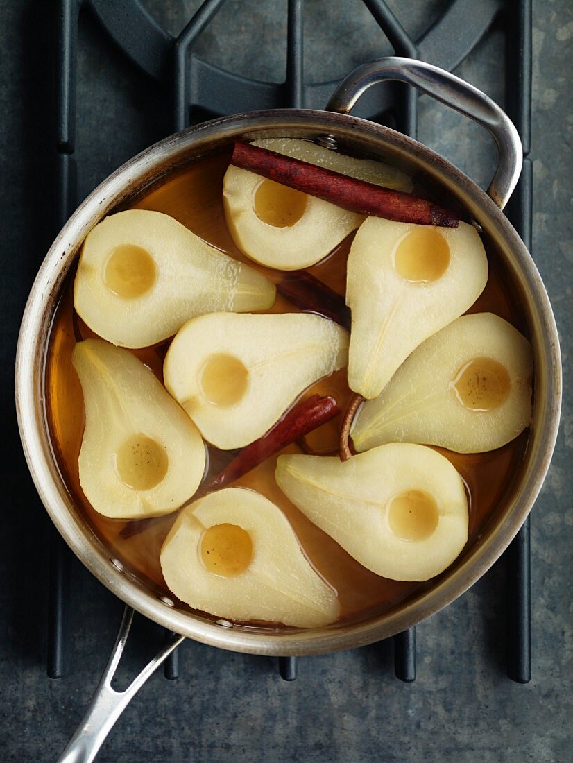 Poached pears with cinnamon sticks in a saucepan