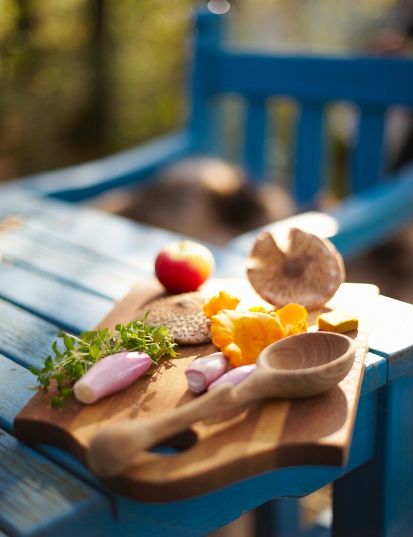 Pilze, Schalotten, Kräuter und Apfel auf Schneidebrett am Gartentisch