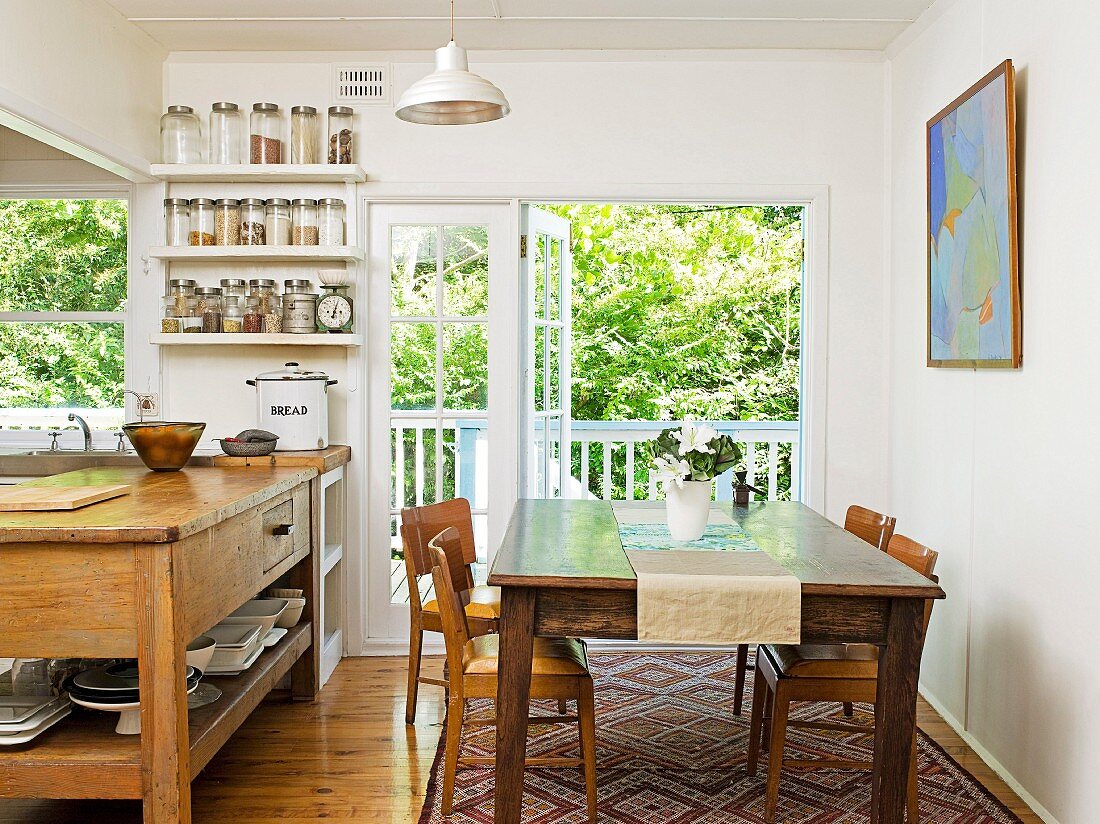 Rustic dining area and counter with shelving in base unit in simple dining room with open balcony door