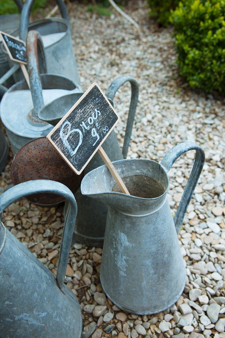 Old zinc jugs with price labels on a gravel path