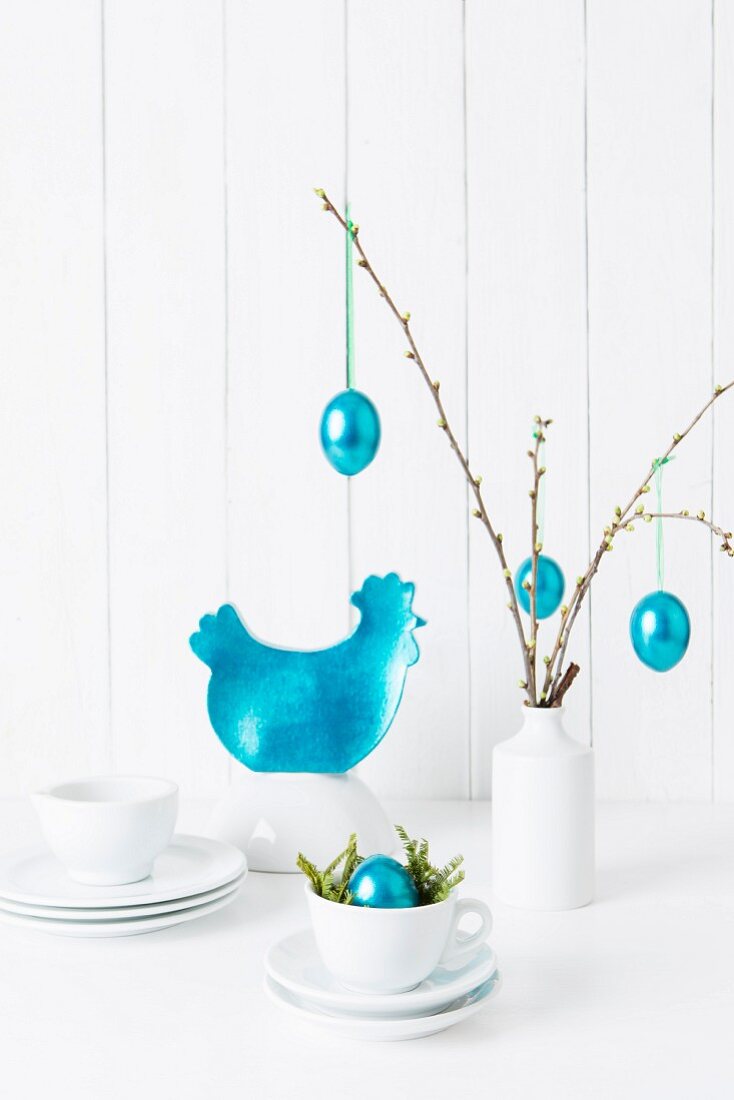 Turquoise Easter decorations and white crockery on a towel against a wooden wall
