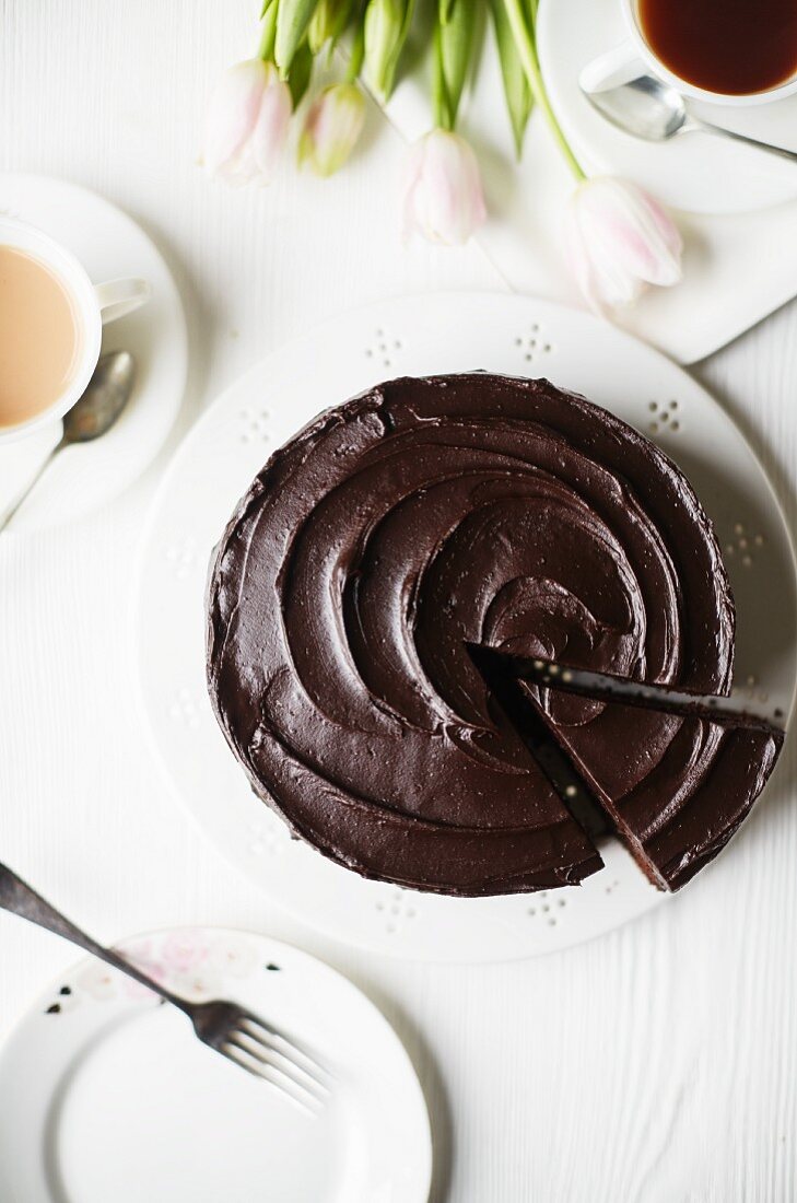 A chocolate cake with a slice cut out and cups of tea