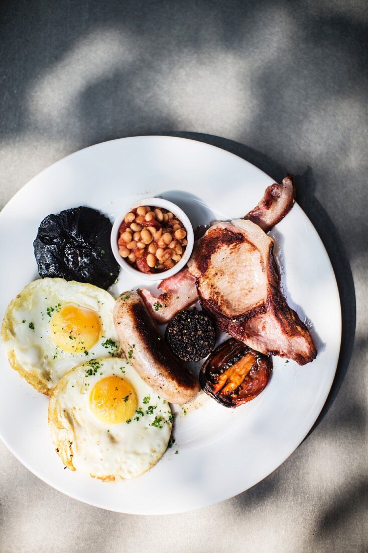 Englisches Frühstück mit Spiegelei, Würstchen, Speck, Blutwurst, Bohnen und gebratenen Tomaten