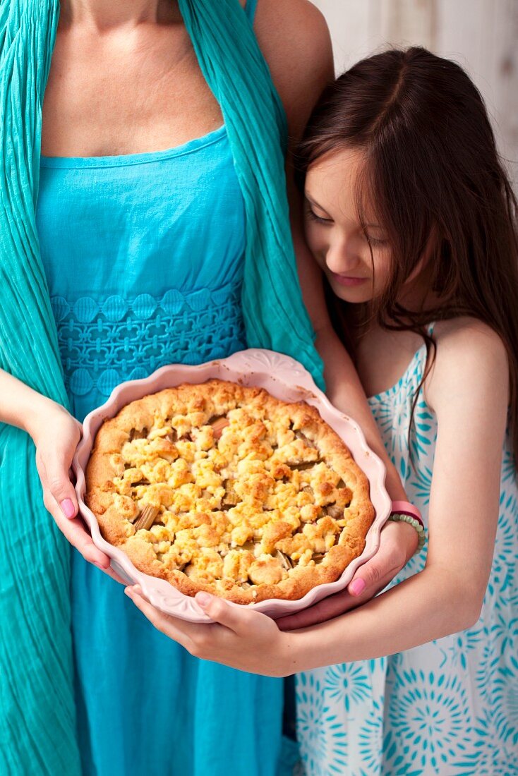 Frau und Mädchen halten Rhabarberkuchen mit Streuseln