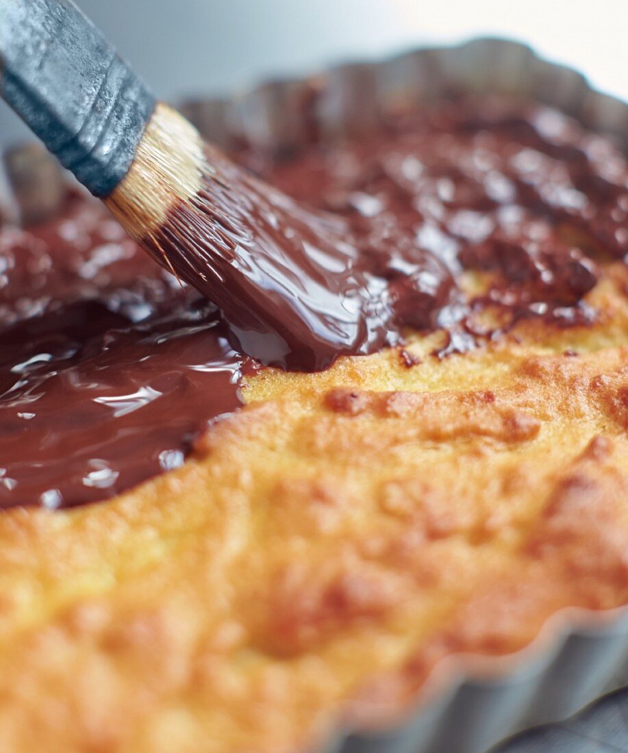 A cake being topped with chocolate glaze