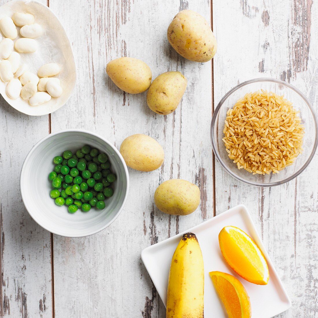 Stillleben mit Erbsen, Kartoffeln, Reis, Bohnen, Banane und Orangen (gute Kohlenhydrate)
