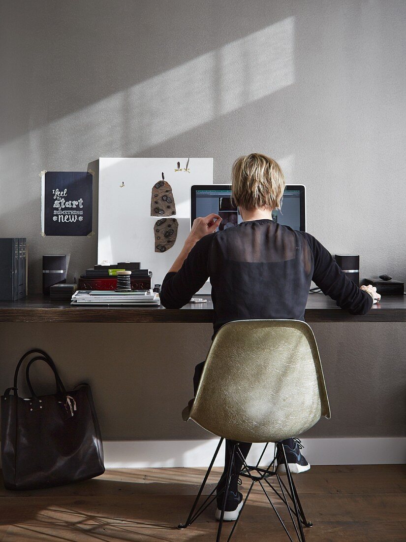Frau auf Eames Stuhl am Schreibtisch in Grau getöntem Homeoffice