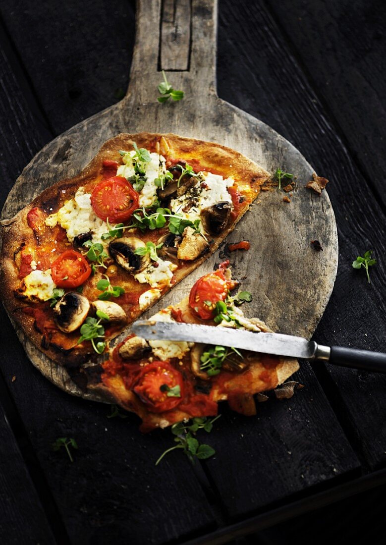 A sliced vegetarian pizza on a wooden pizza paddle