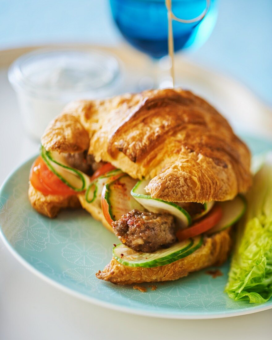 A croissant sandwich with spicy meatballs, cucumber and tomato