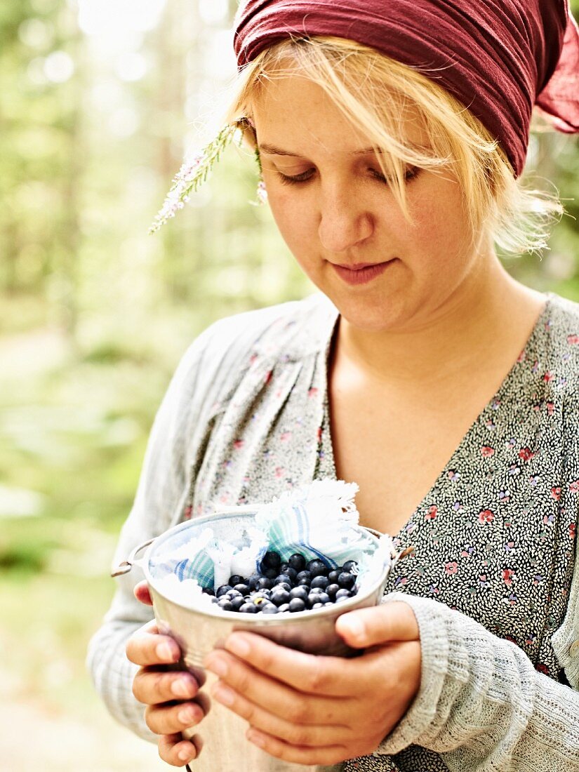 A girl holding a small bucket of freshly picked blueberries