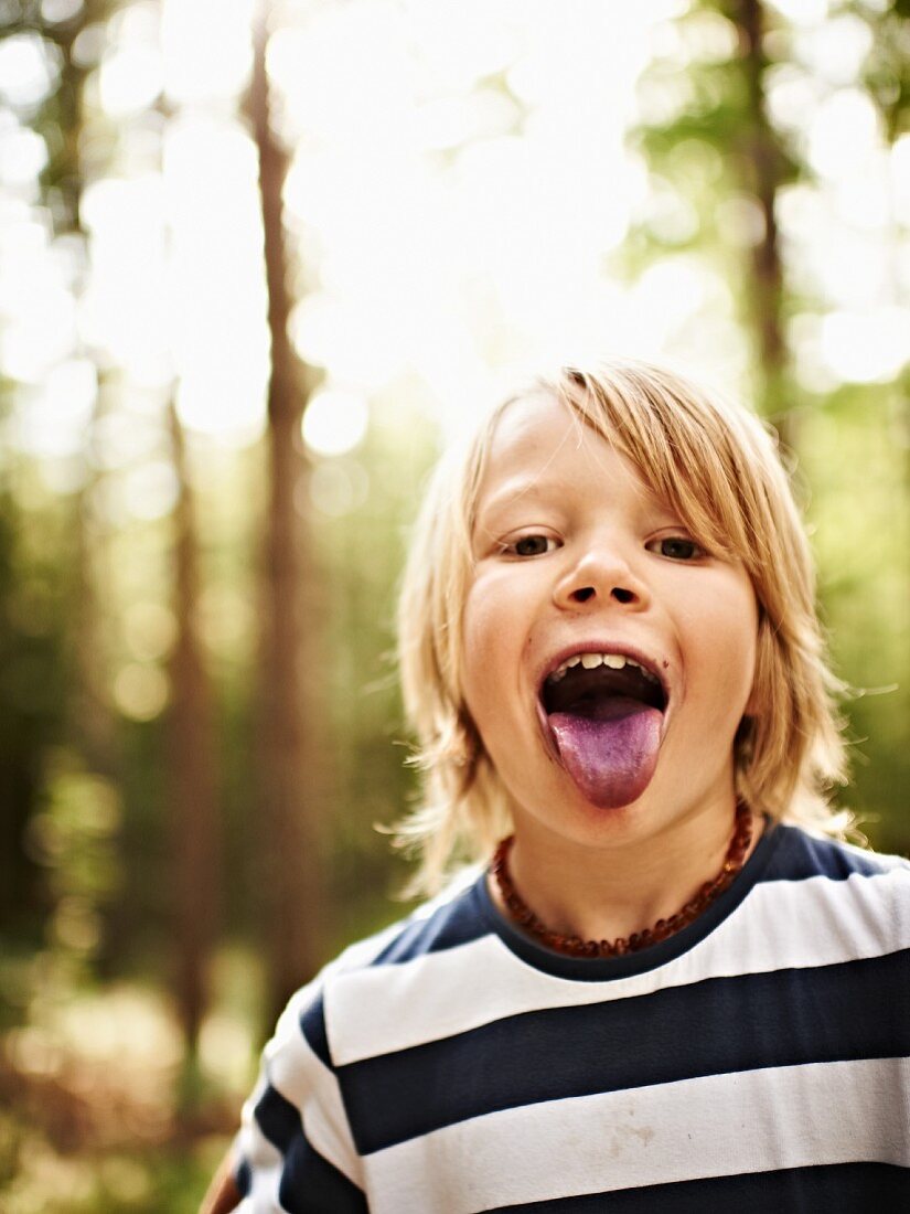 Junge im Wald streckt blau gefärbte Zunge heraus