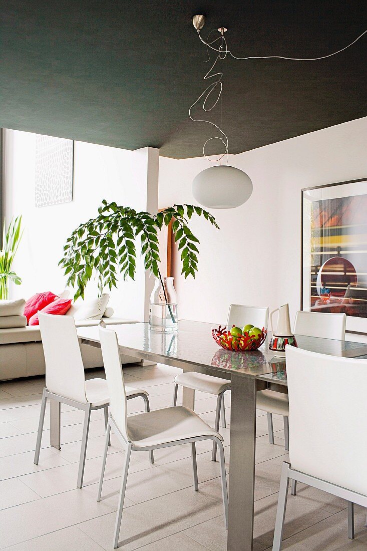 Designer dining area decorated with leafy branch in glass vase and white pendant lamp hanging from black ceiling