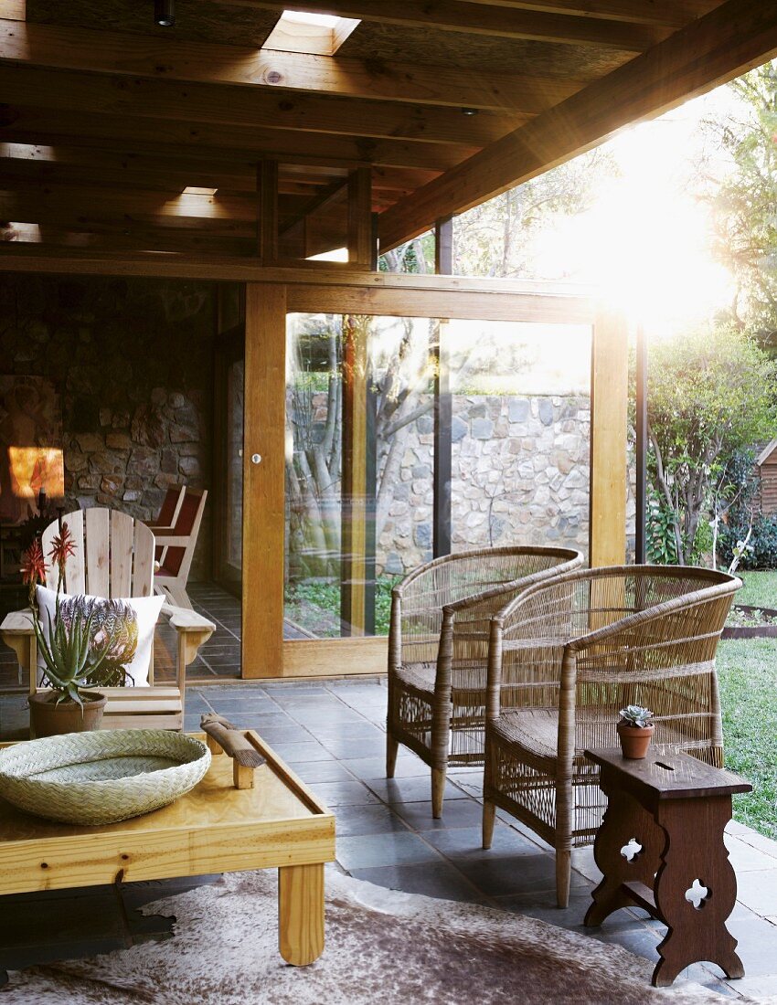 Roofed terrace integrated into house with armchairs, wicker chairs and side table on animal-skin rug; sliding door in front of interior in background