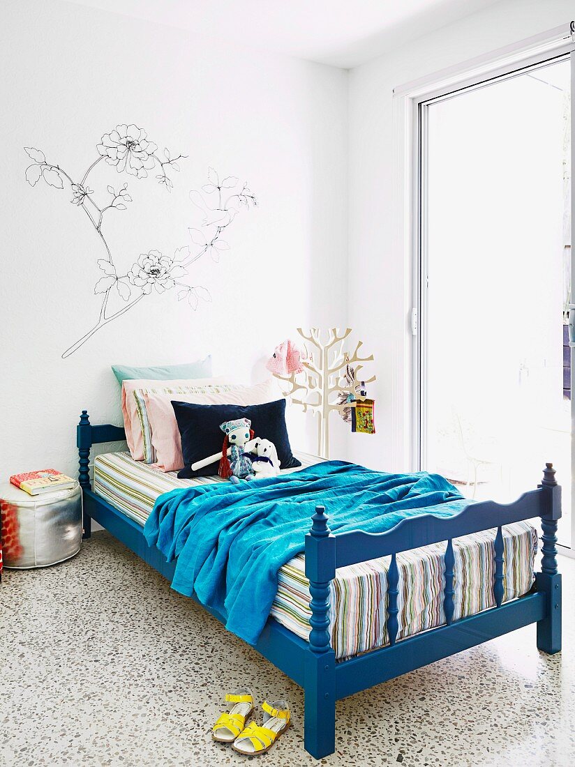 Pflanzenzeichnung auf Wand über blau lackiertem, gedrechseltem Kinderbett; stilisierter Baum zum Aufhängen von Utensilien im Hintergrund