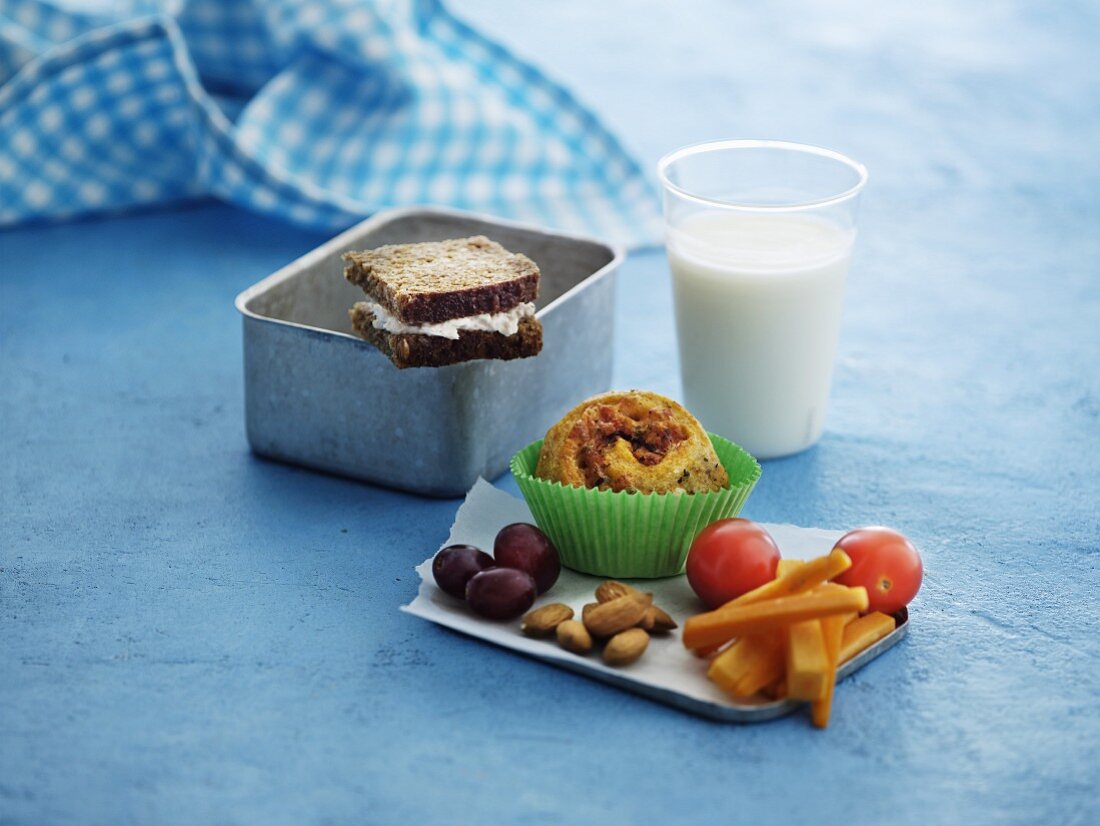 A sandwich, muffins, vegetables, grapes, almonds and milk for lunch