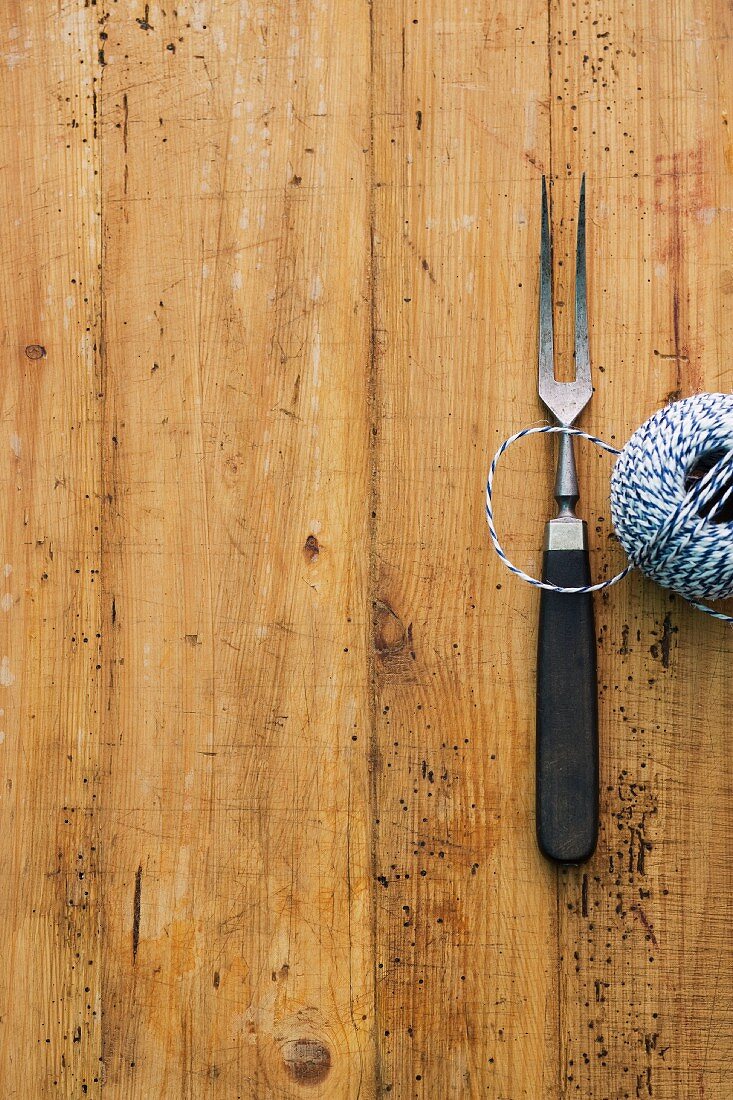 A carving fork and kitchen twine on a wooden surface