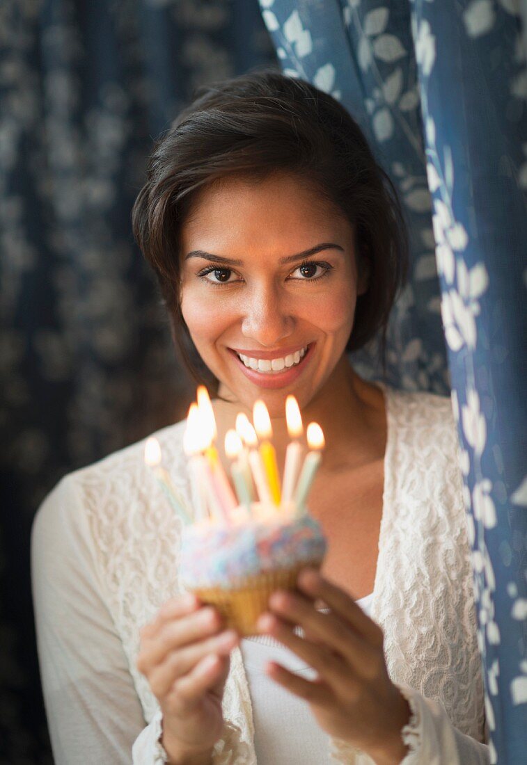 Dunkelhaarige Frau hält Geburtstagstörtchen mit Kerzen
