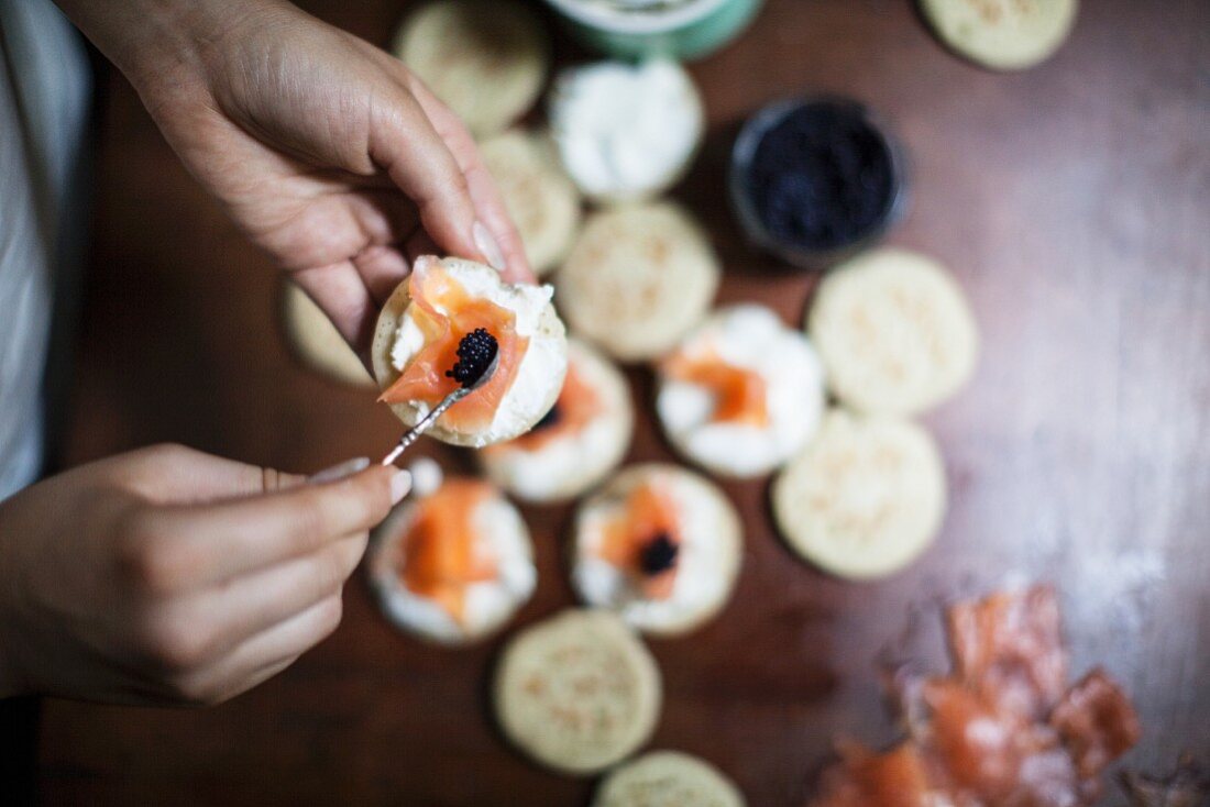 Blinis being topped with salmon and caviar