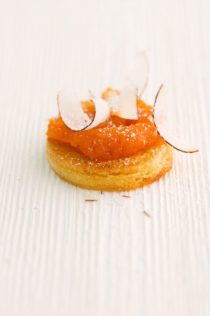A round slice of bread topped with carrot and passion fruit spread and grated coconut